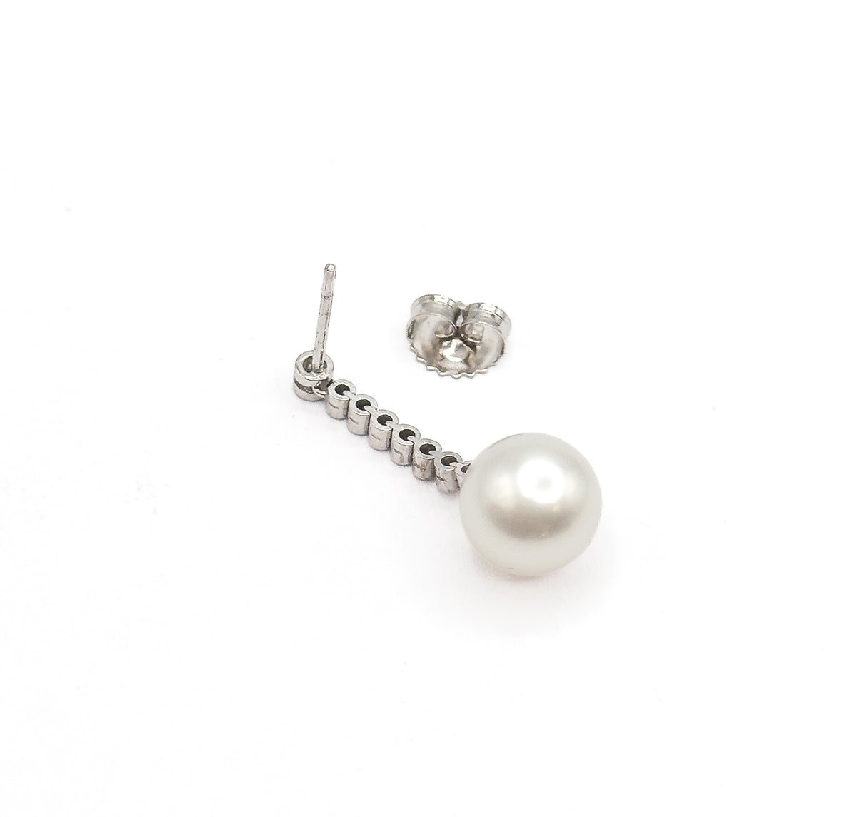 A single earring laid flat on white beside its detached butterfly back, showing the straight post, the row of bezel-set round diamonds and the creamy pearl at the end.