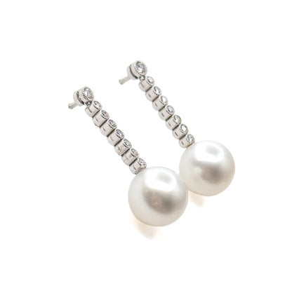 Viewed from above with the pair set close together, the two creamy pearl drops overlapping in the foreground while the diamond lines recede behind toward the slim posts.