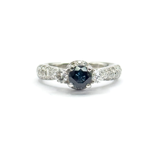 Contemporary sapphire and diamond three-stone ring in platinum, shown upright face-on against white, the deep blue sapphire in a tall prong basket between two round diamonds, with pavé shoulders.