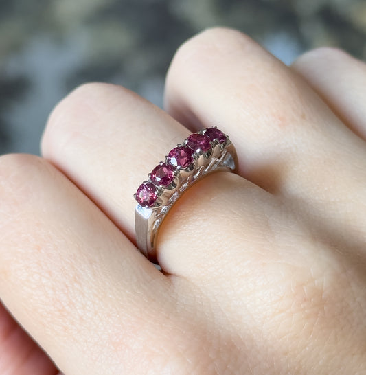 Shown on a finger at an angle, the row of rubies seen close up with the tall open baskets and pierced gallery standing well above the white gold shank.