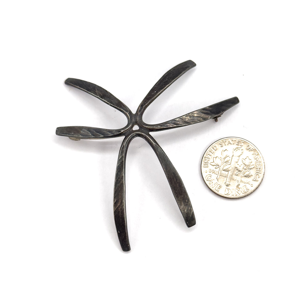 The brooch lies beside a dime on white, the coin reaching only a fraction of one ray's length, giving a clear sense of the starburst's generous scale.