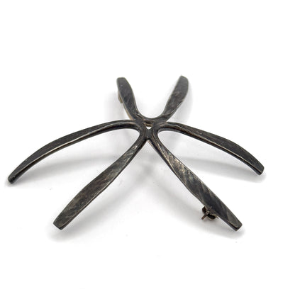 Angled back view from the tip end, the rays lifting and curving away from the flat plane so the starburst's sculptural depth shows, with the coiled hinge and catch at opposite ray tips.