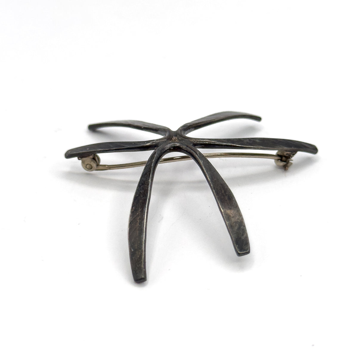Low edge-on view from the back, two rays sweeping down toward the viewer while the pin stem runs level behind them, showing how far the silver lifts off the flat plane.