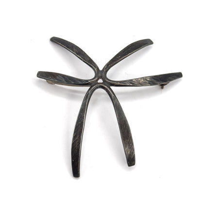 Straight-on back view where the five rays meet at a small central opening, the hammered facets along each ray catching light while dark patina sits in the recesses, pin stem crossing behind.