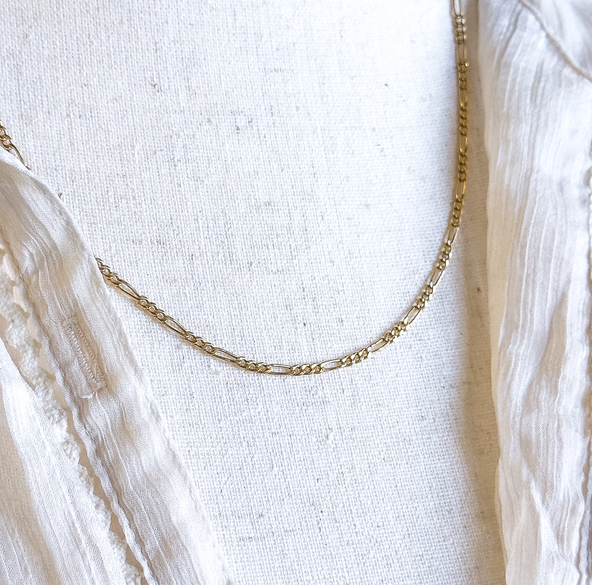 The chain's full curve sweeps across the woven cream bust form here, rising steeply up the right side toward the shoulder with a short length also visible at the far left edge.