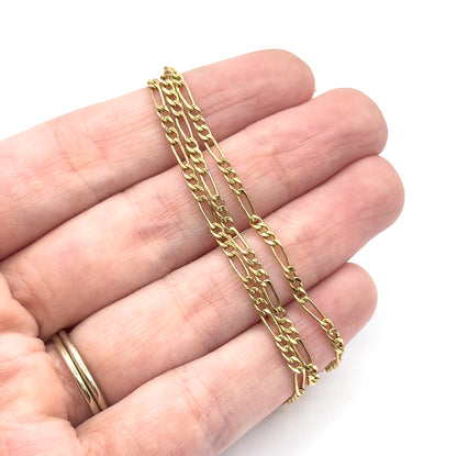 The chain is draped in doubled strands across an open palm, giving a clear sense of its fine width and light weight, with the alternating round and long links spanning two fingers.