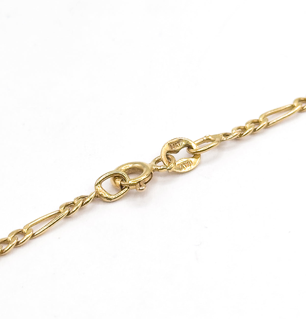 Close-up of the spring ring clasp and its stamped round tag beside the oval jump ring, with the Figaro links running off to each corner against a white background.