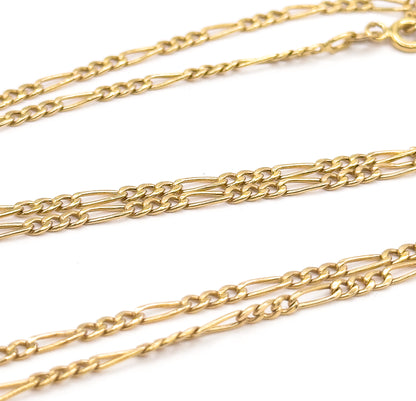 Three diagonal runs of the Figaro chain cross the frame at an angle, the polished links sharpest in the middle row while the spring ring clasp sits small and blurred at the top right corner.