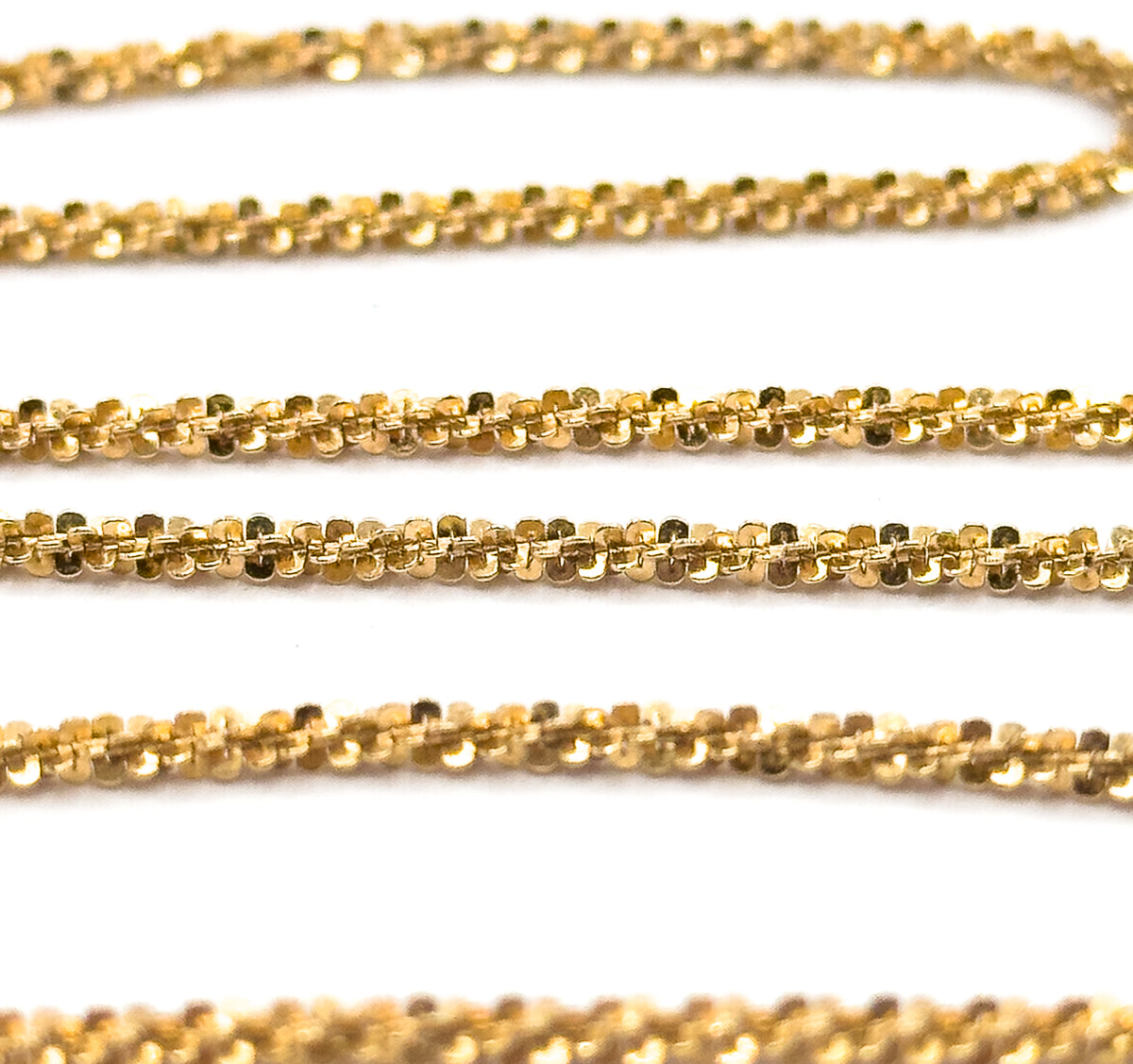Extreme close-up filling the frame with several rows of the chain, revealing each tiny faceted popcorn link nestled against the next along the twisted yellow gold rope.
