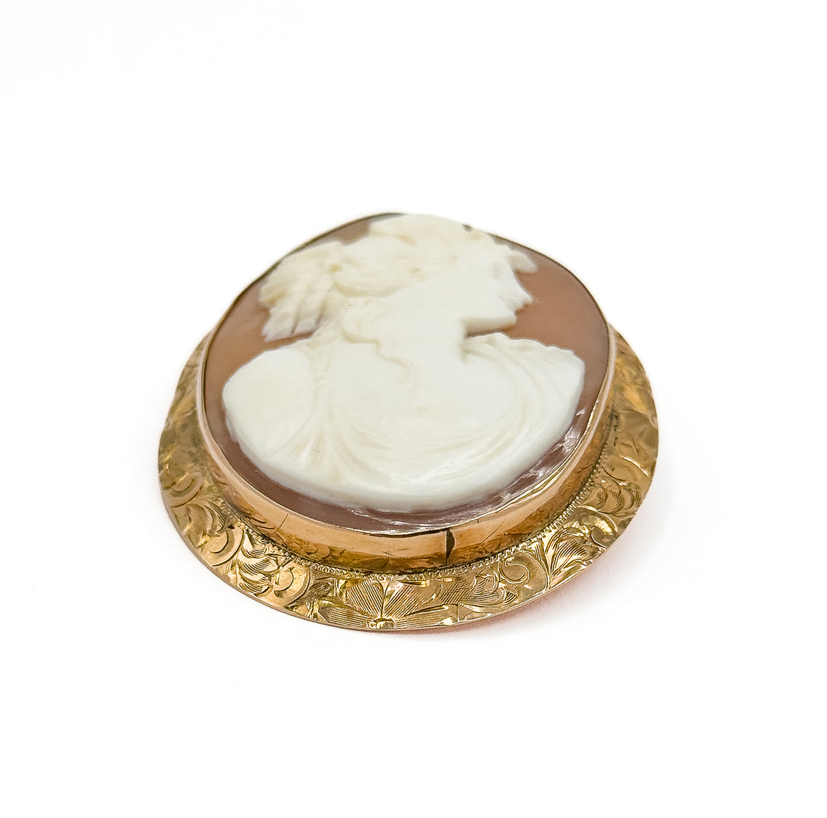 Angled from the lower side, the cameo tipped away so the shell portrait recedes while the engraved floral gold band curves wide across the front like a shallow dish.