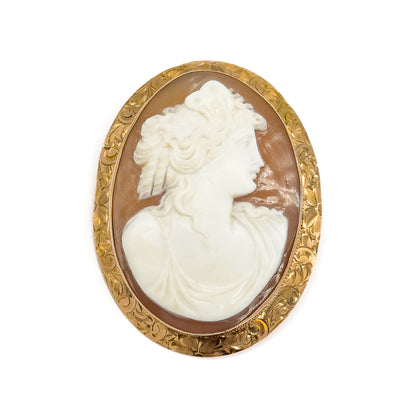 Straight-on face-up view filling the frame, the creamy white profile and caramel brown background of the shell cameo fully visible inside the plain bezel rim and engraved floral gold band.