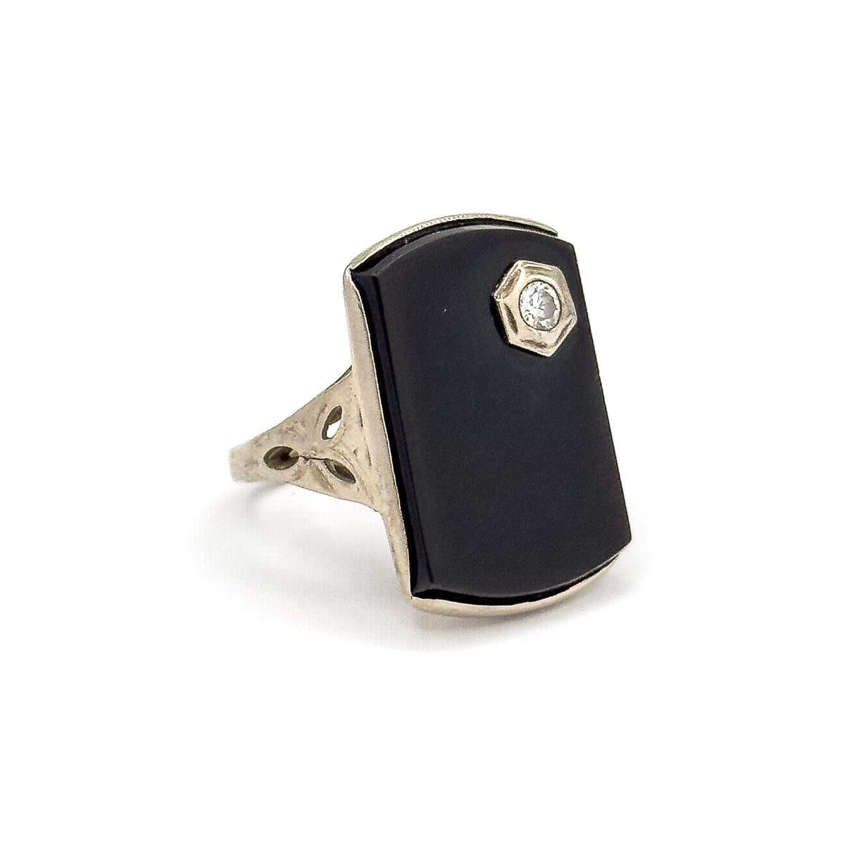 Three-quarter front view showing the full elongated black onyx face with the small round diamond in its hexagonal bezel near the top corner, above the pierced leaf-etched shoulder.