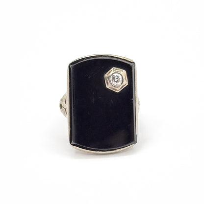 Straight-on front view against white, the tall black onyx face filling the frame with the small round diamond in its hexagonal bezel at the upper right, shoulders just visible either side.