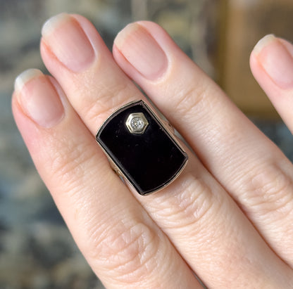 Close overhead view on the hand, the onyx face filling the finger from knuckle to knuckle with the small hexagonal diamond bezel just above centre.