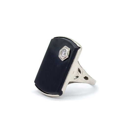 Angled side view against white, showing the onyx face in profile with its white gold bezel edge, the hexagonal diamond setting, and the pierced shoulder with etched leaf cutouts meeting the shank.