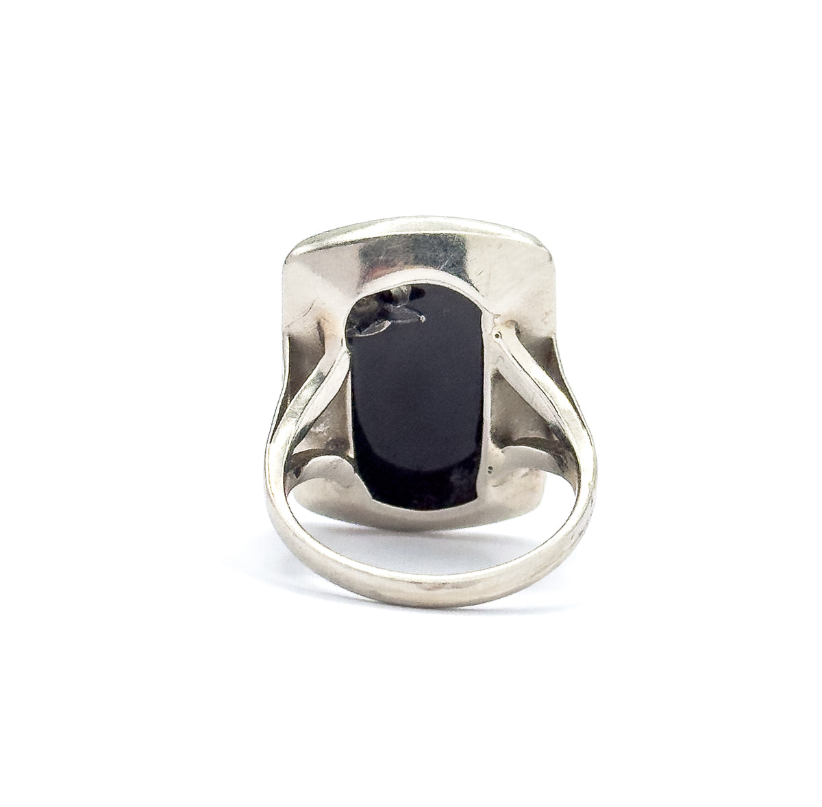 Back of the ring stood upright against white, the open gallery revealing the underside of the black onyx slab and the smooth inner bezel wall, the slim round shank curving below.