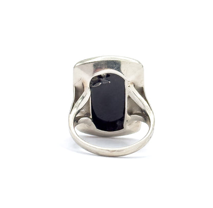 Back of the ring stood upright against white, the open gallery revealing the underside of the black onyx slab and the smooth inner bezel wall, the slim round shank curving below.