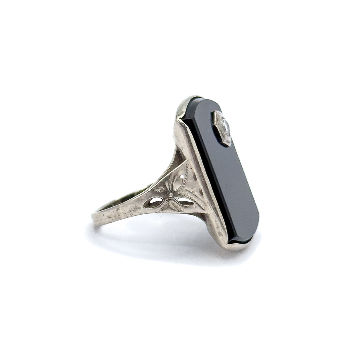Steep side view with the onyx slab standing tall on edge, its bezel lip catching light along the top corner while the leaf-etched shoulder and shank taper away below.