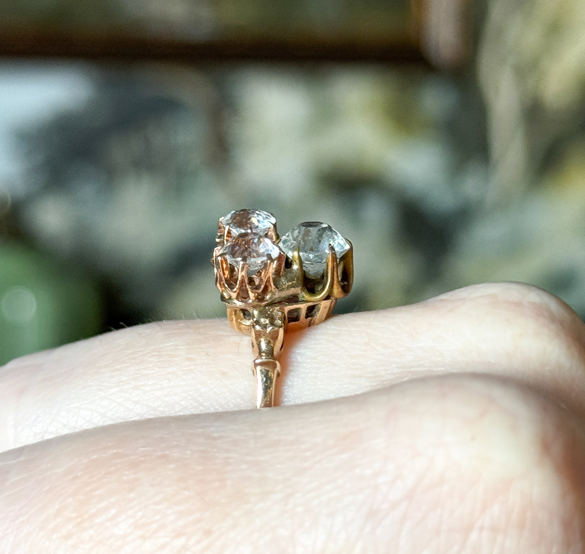 Close side profile on the finger, showing the three prong baskets clustered and soldered side by side above the tapering shank, with the stones catching light from above.
