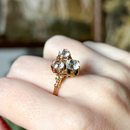 Angled from above on the hand, the three stones read as a triangular cluster, with open gallery work visible beneath the baskets and the shank running down between the knuckles.