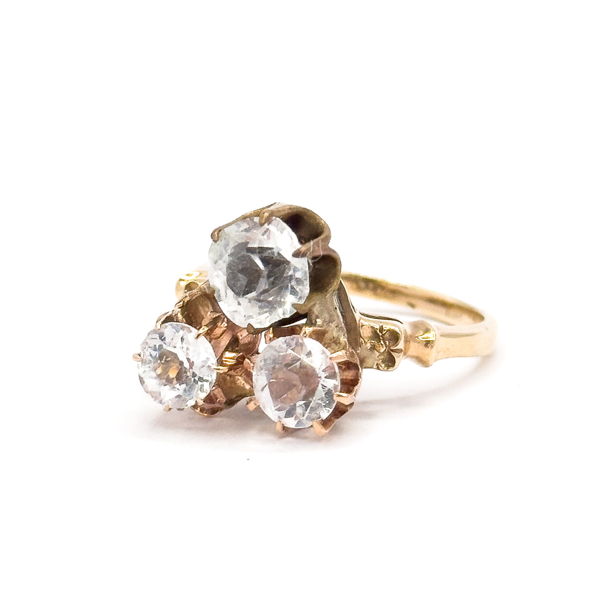 Off the hand against white, the ring stands in profile so the three prong baskets rise clear of the shank, with orange blossom detailing visible where the shoulders meet the band.
