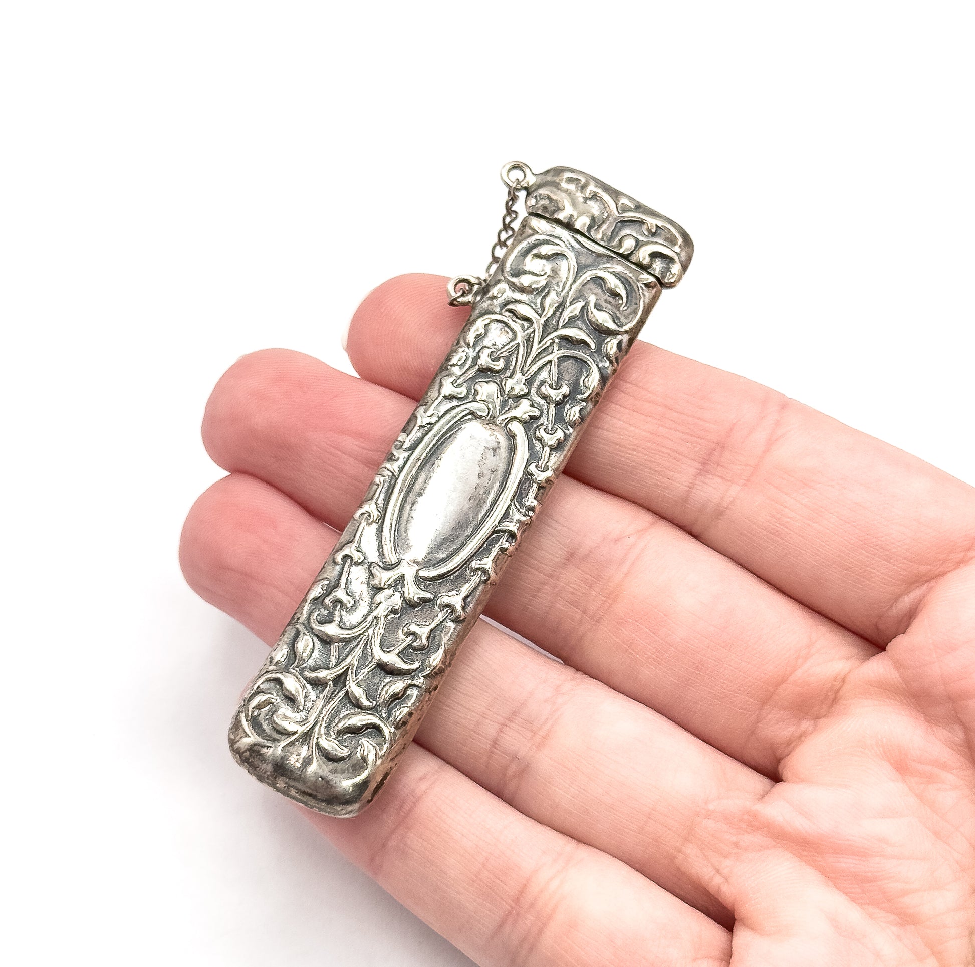 Resting across the open fingers of a hand, which gives its scale, the case spans about the width of four fingers, cap at top with its chain looping free.