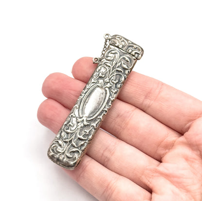 Resting across the open fingers of a hand, which gives its scale, the case spans about the width of four fingers, cap at top with its chain looping free.