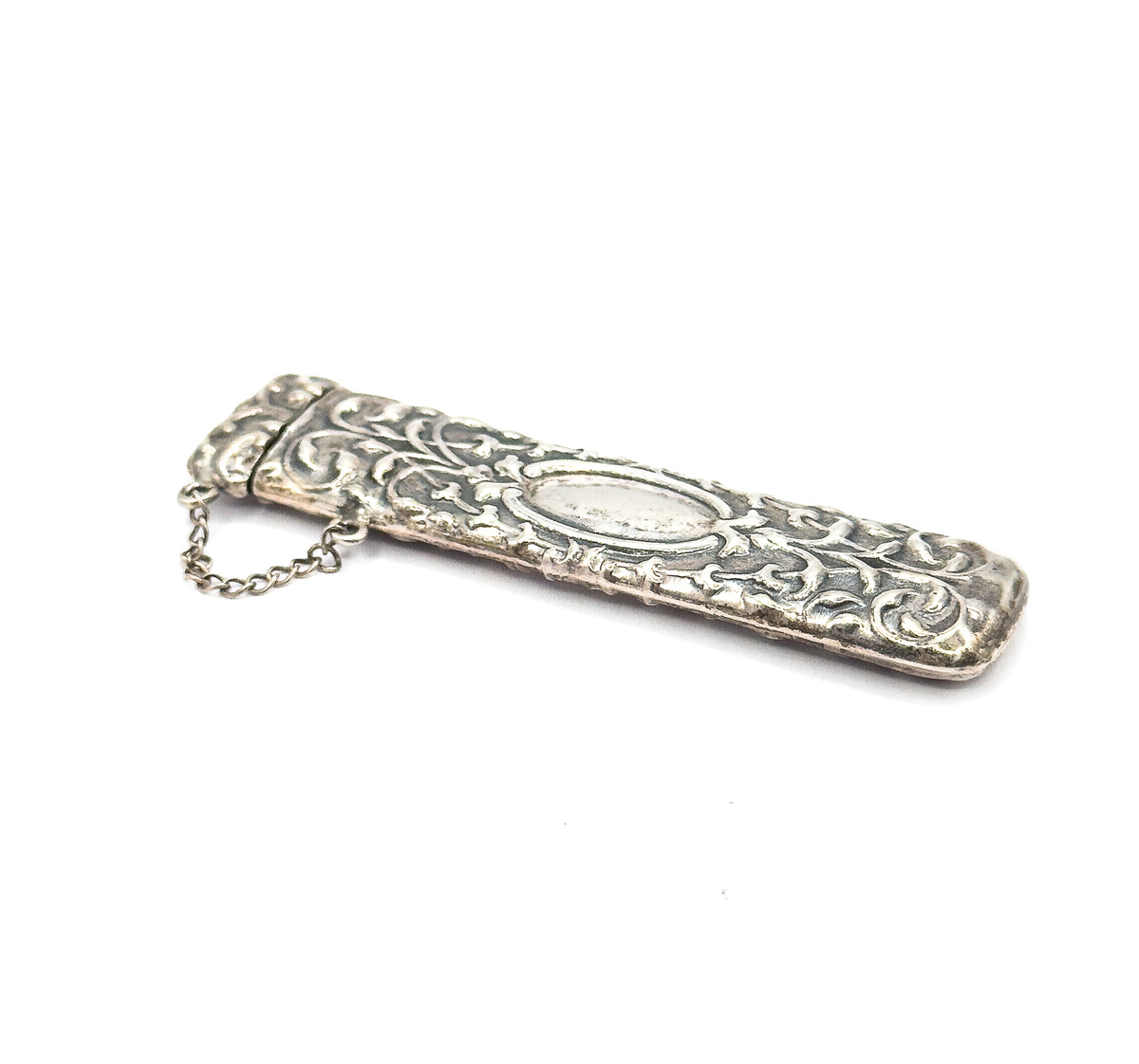 The case seen from above at a steep diagonal on white, cap end nearest the viewer with the chain curving loose beside it, the plain oval panel and darkened patina in the scrollwork clear.