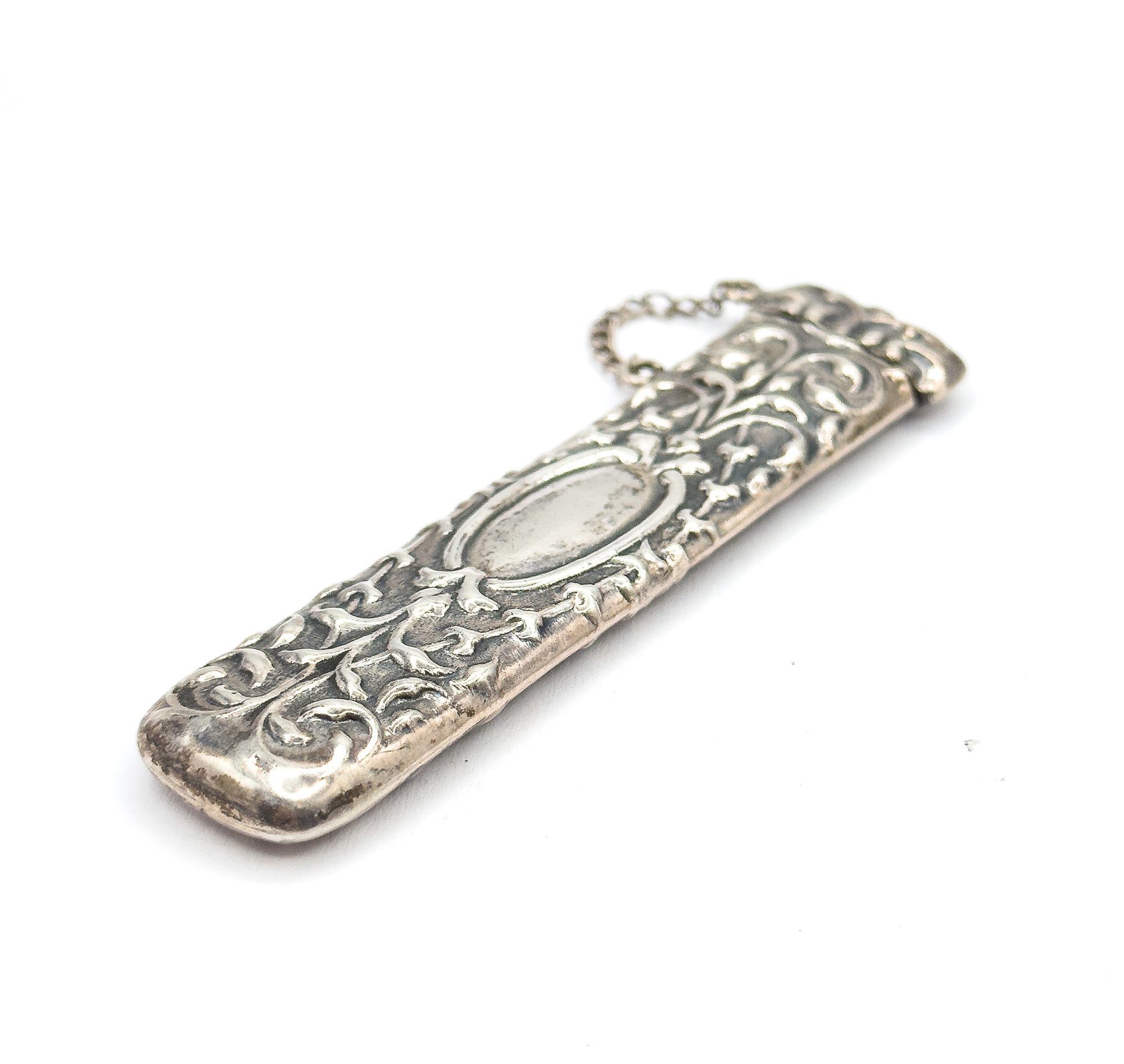 The case angled diagonally with its rounded base closest to the viewer, so the sterling silver scrollwork tapers away toward the cap and chain at the far end.