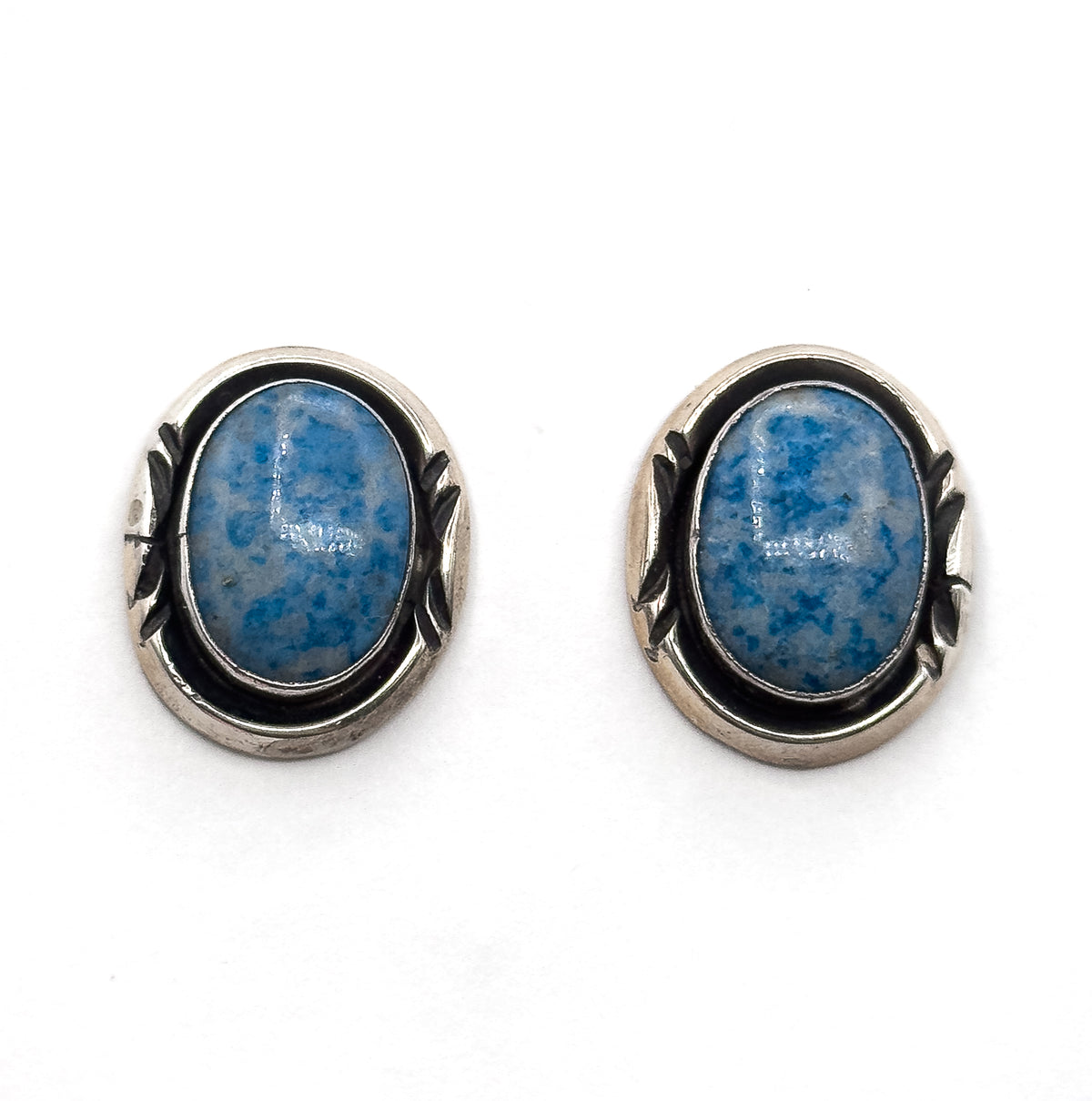 The pair side by side face up on a plain white background, straight on, showing both oval cabochons and the darkened silver surrounds with their leaf-shaped side detail matching each other.