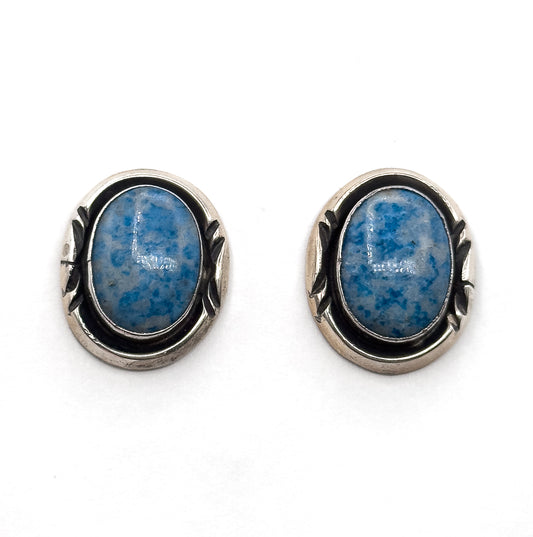 The pair side by side face up on a plain white background, straight on, showing both oval cabochons and the darkened silver surrounds with their leaf-shaped side detail matching each other.