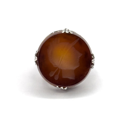 Straight-on top view filling the frame with the round rootbeer quartz, the right-facing soldier intaglio clearly readable between four leaf-shaped sterling silver prongs.