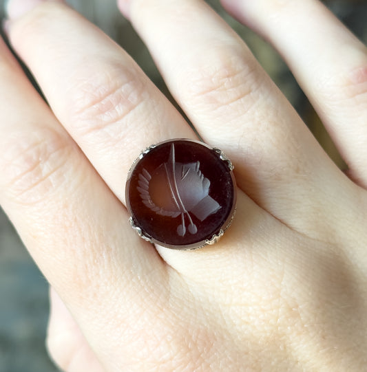 Close overhead view on the hand, the round rootbeer stone spanning almost the full width of the finger, with four decorative prongs gripping its edge.
