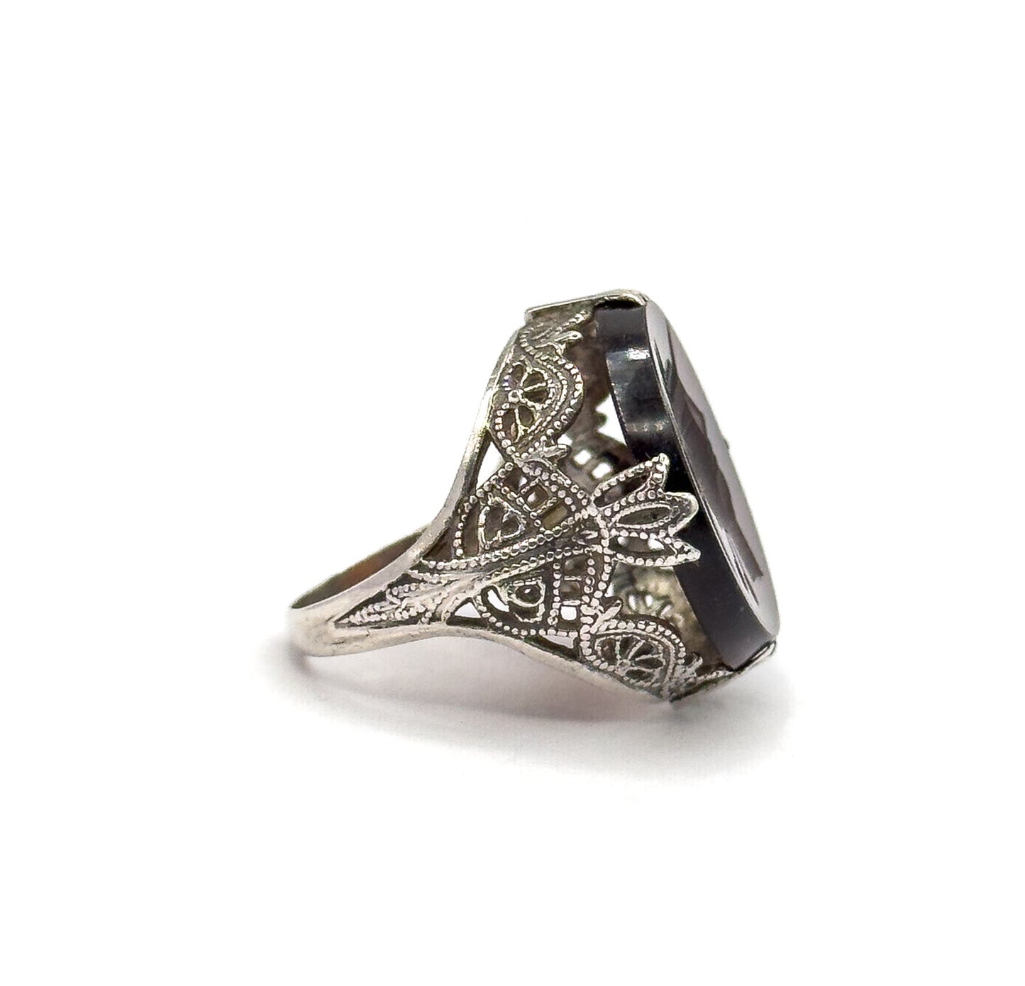 Side profile against white showing the deep gallery wall of scrolled die-stamped filigree, the tapering shank, and the stone standing tall on edge within its prongs.