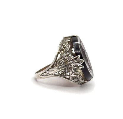 Side profile against white showing the deep gallery wall of scrolled die-stamped filigree, the tapering shank, and the stone standing tall on edge within its prongs.