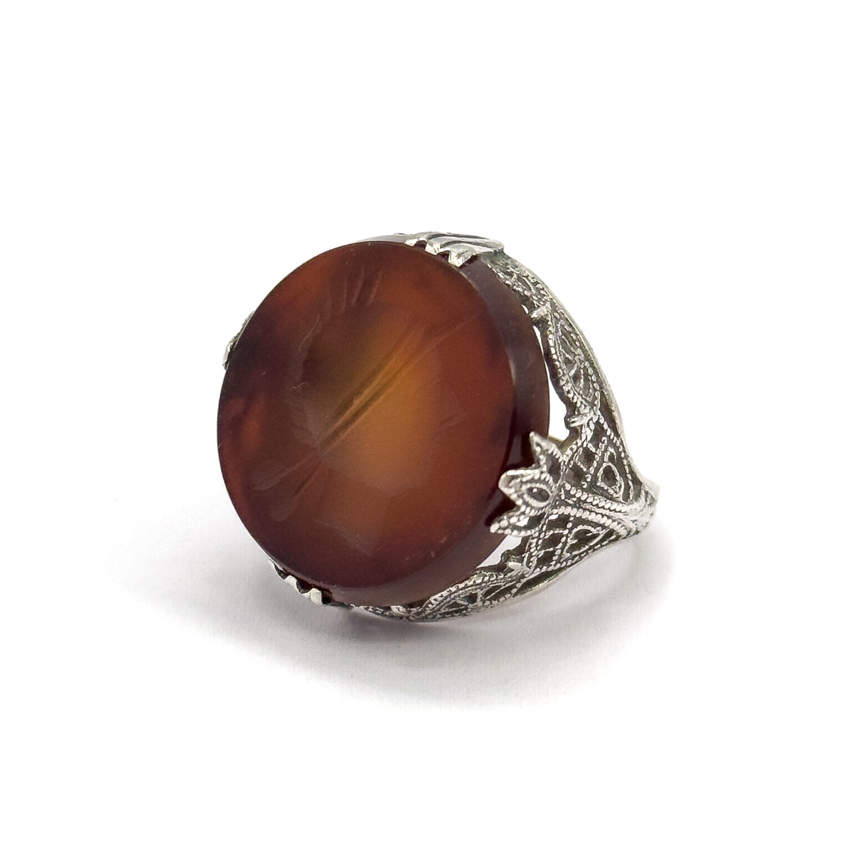 Angled three-quarter view with the round rootbeer quartz tilted toward the camera, the carved intaglio soldier profile catching light across its face above the filigree shoulder.
