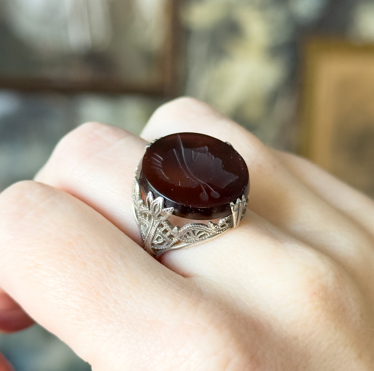 Vintage intaglio carved quartz ring in sterling silver, shown on a finger, the round deep rootbeer stone carved with a right-facing soldier profile above a filigree gallery and prongs.