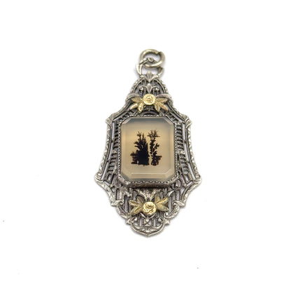 Full-length front view showing the whole tall, narrow silhouette from the upright open jump ring at the top down to the pointed filigree tip, with both applied gold flowers framing the bezel-set stone.