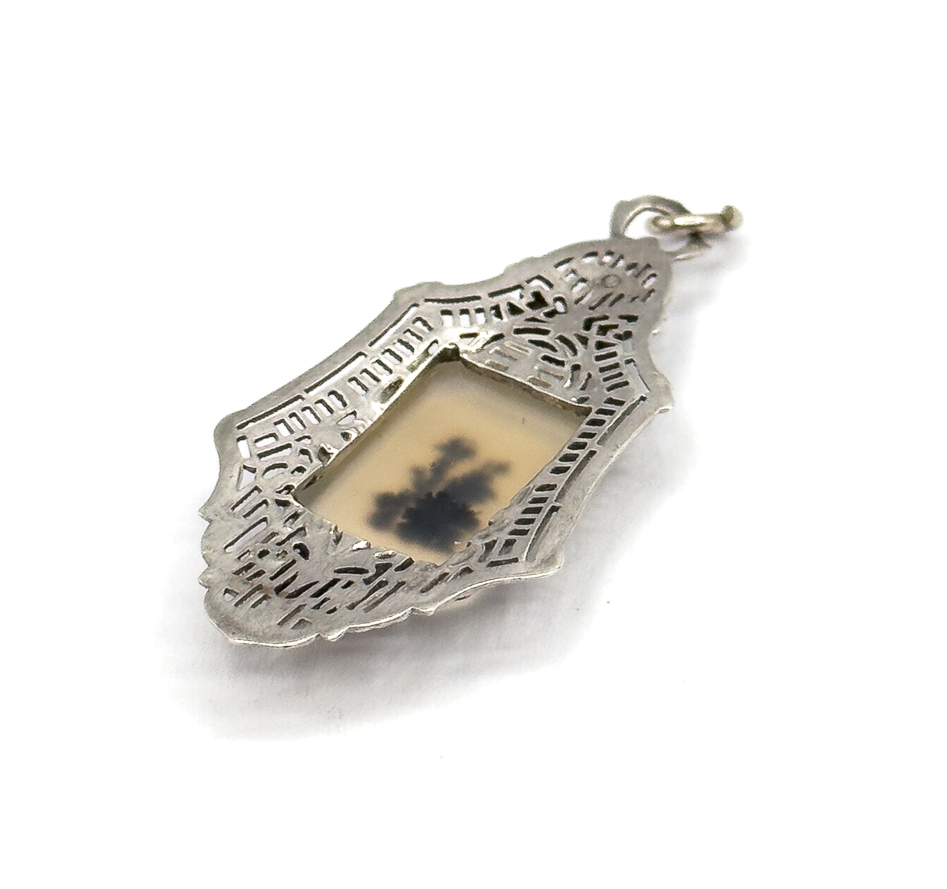 Tilted three-quarter view on white, the lozenge frame's pierced filigree catching light along its raised edge, with the pale stone and its dark fernlike markings set deep in the bezel below the bail.