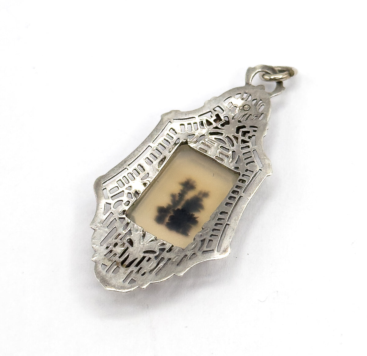 Angled from the reverse, the open jump ring stands proud at the top and the piercing shows as open cut-outs right through the frame around the bezel-set pale stone.