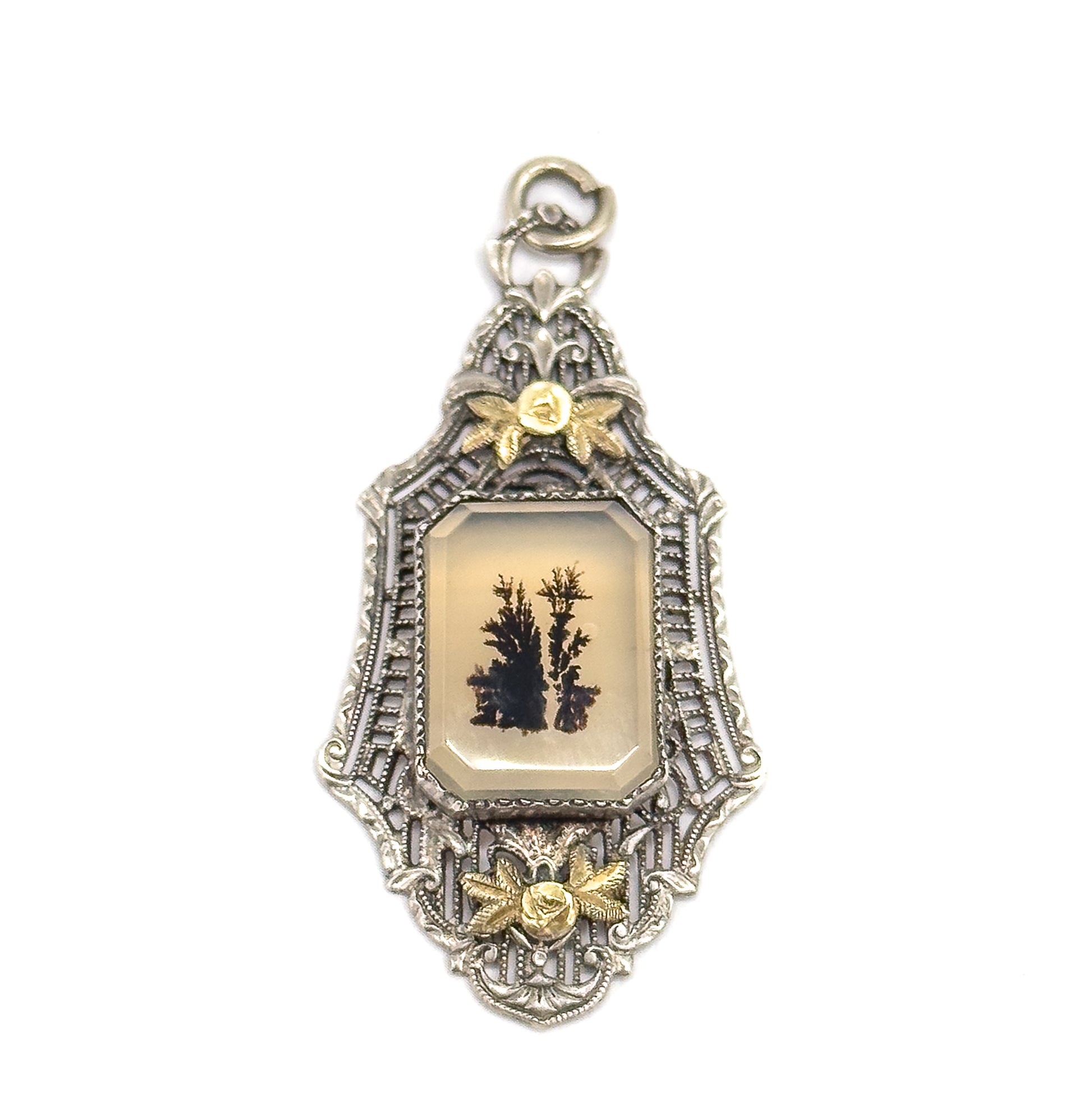 Straight-on front view on white, the pale bezel-set stone with its dark fernlike markings centred in the filigree frame between an applied gold flower above and another below the setting.