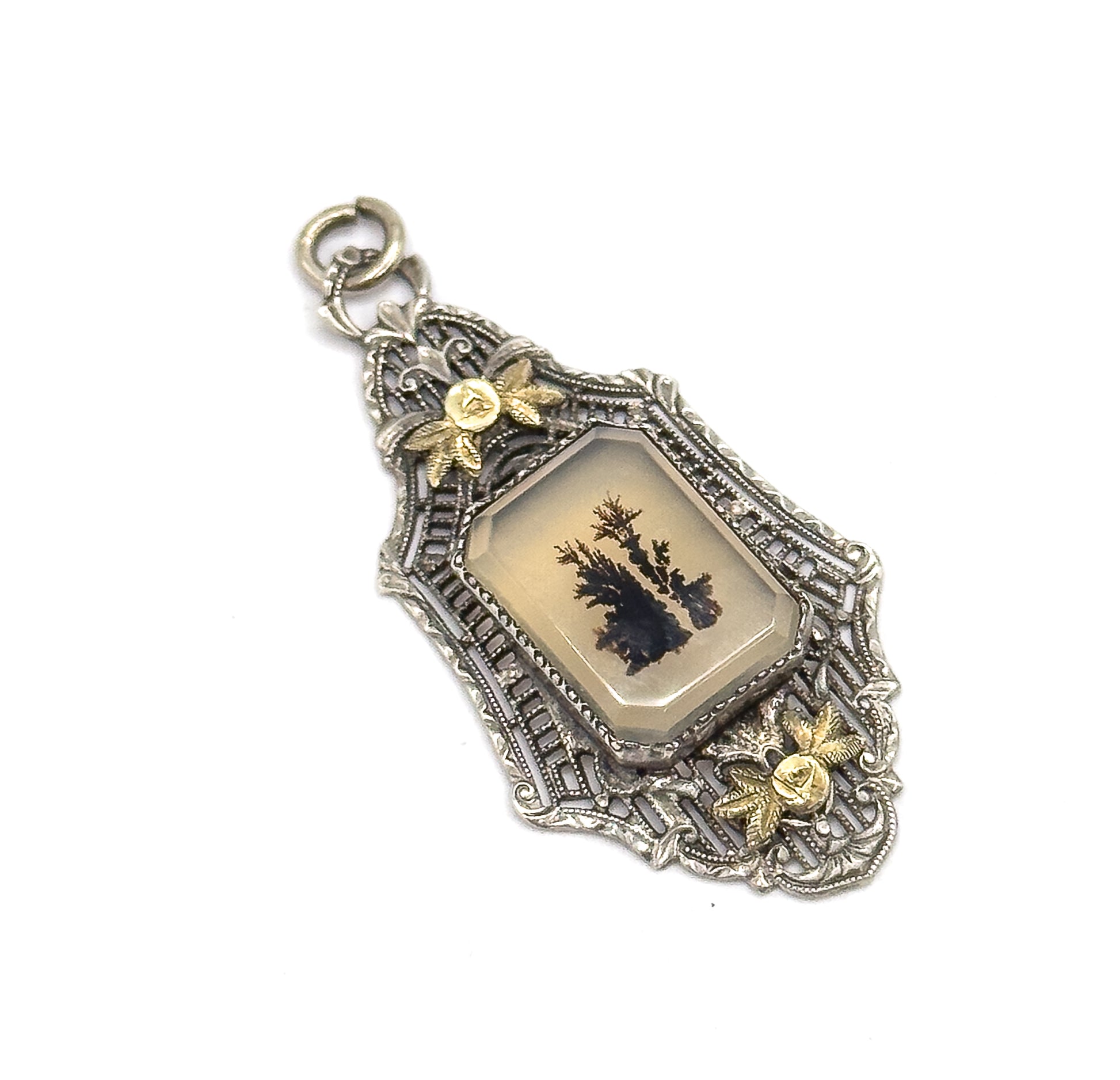 Diagonal view with the open jump ring at top left, its gap clearly visible, the beveled stone's angled corners and the scrolled filigree edges standing out between the two applied gold flowers.