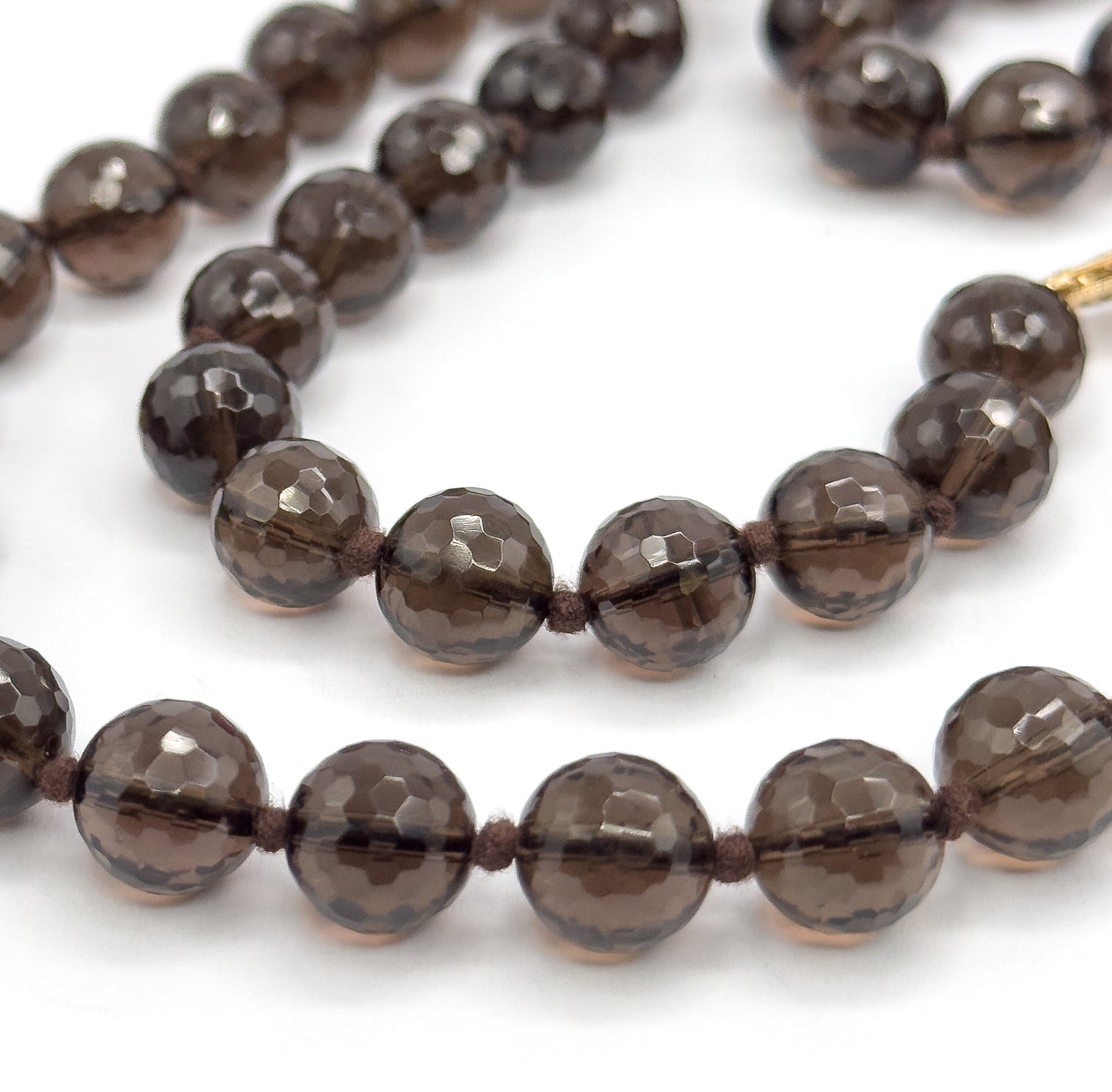 Two curving rows of faceted smoky quartz beads fill the frame, with just the tip of the gold clasp entering at the upper right and knots visible between every bead.