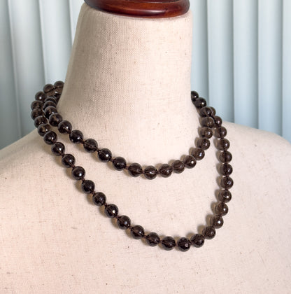 Shown at the neck on a linen dress form, the strand doubled into two rows of deep brown faceted beads sitting close to the collarbone.