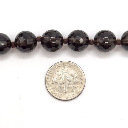 A close view of a single row of faceted smoky quartz beads with knots between them, a dime placed below for scale, each bead a little wider than the coin is thick.