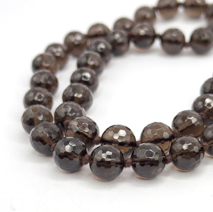 A tight macro of the strand curving in two rows on a white surface, showing the many small flat facets on each deep brown bead and the fine knots tied between them.