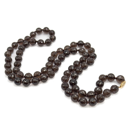 The whole necklace laid flat on white in a loose looping coil, showing its full length of knotted faceted smoky quartz beads and the small gold clasp at the right-hand end.