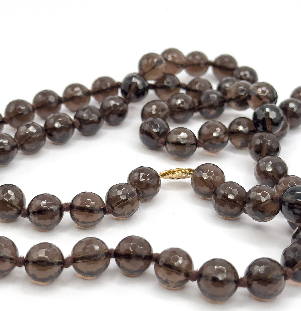 The coiled strands photographed close in, with the small patterned gold clasp lying flat between two rows of faceted deep brown beads and their knots.
