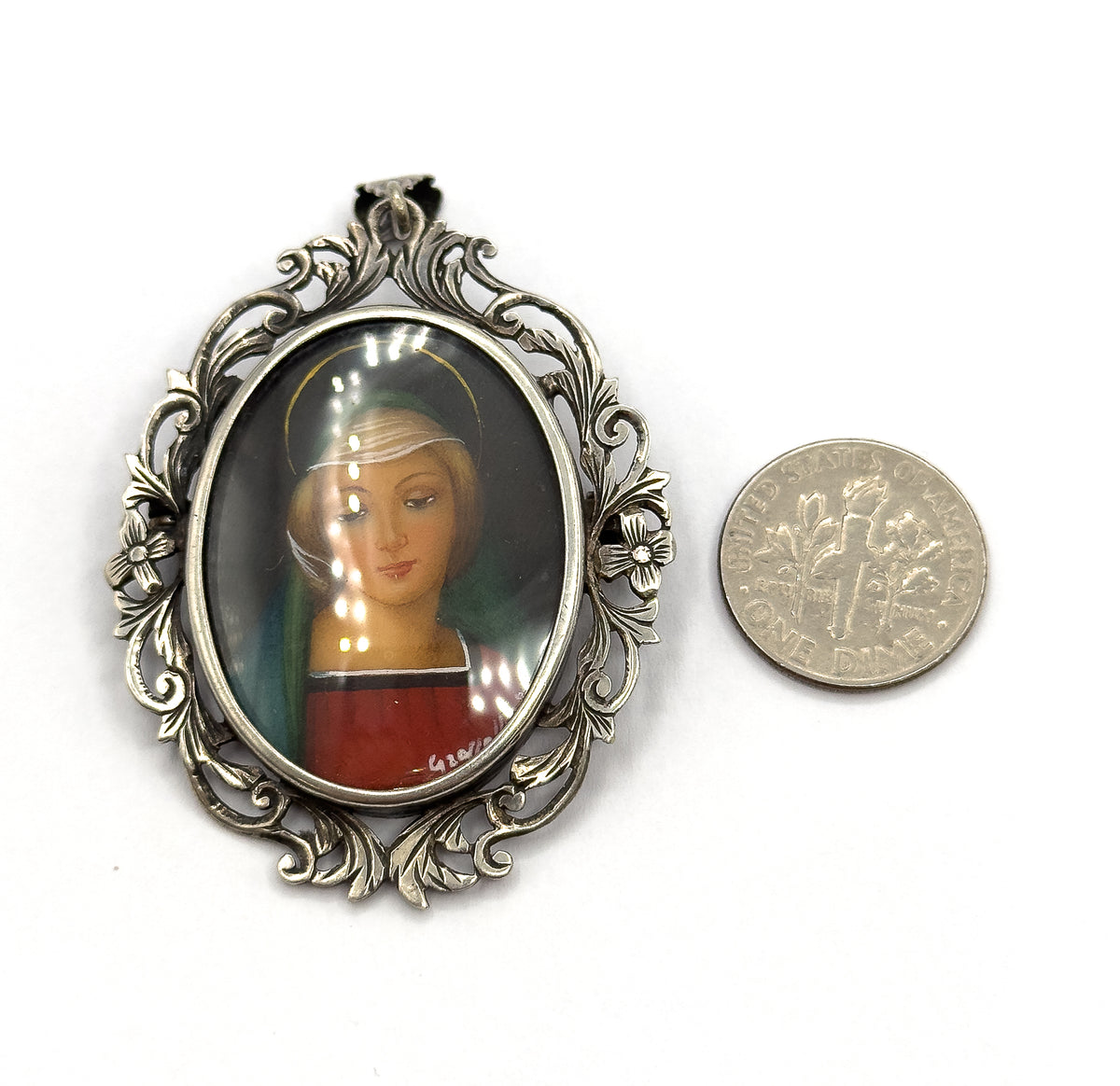Shown face-up on white beside a US dime for scale, the oval glass-covered portrait and its scrolling acanthus frame standing about twice the coin's width tall.