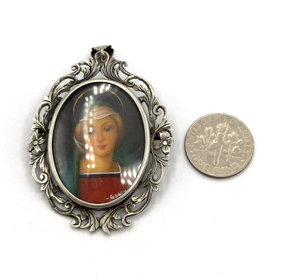 Shown face-up on white beside a US dime for scale, the oval glass-covered portrait and its scrolling acanthus frame standing about twice the coin's width tall.